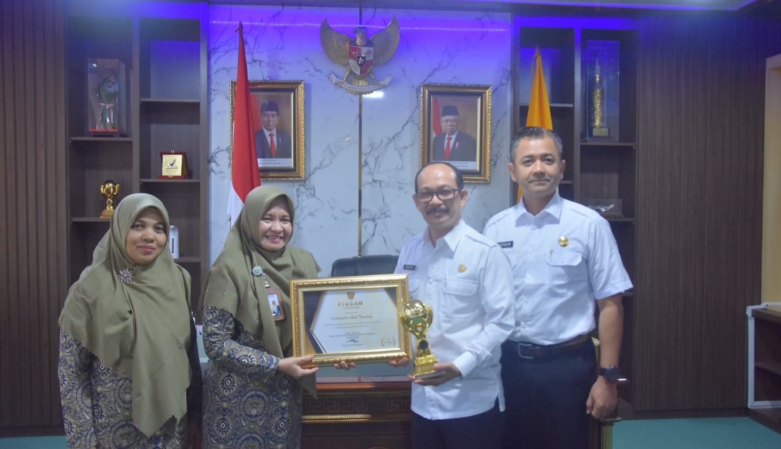 Pj. Bupati Aceh Tamiang, Dr. Drs. Meurah Budiman, SH, MH, didampingi Kepala Dinas Kesehatan, dr. Mustakim menerima piala dan piagam Universal Health Coverage yang diserahkan melalui Kepala Cabang BPJS Langsa, Sri Yulizar Pohan. Dok : Prokopim/SWARA45.COM]